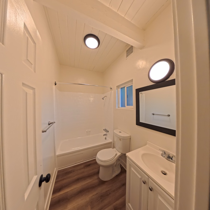 Bathroom with a tub and shower, white vanity, black-framed mirror and a white wood ceiling