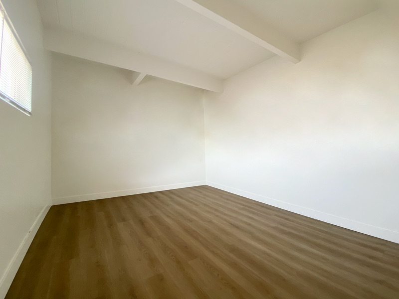 Empty bedroom with a window, white walls, a beamed ceiling and wood-look plank flooring