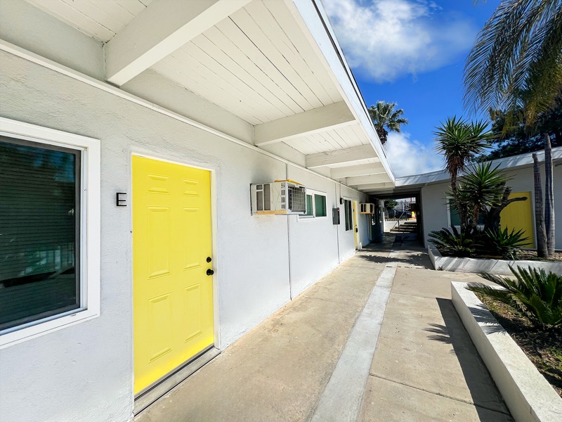 Covered walkway at Rock Ridge with yellow unit doors, white walls and raised planters with palms