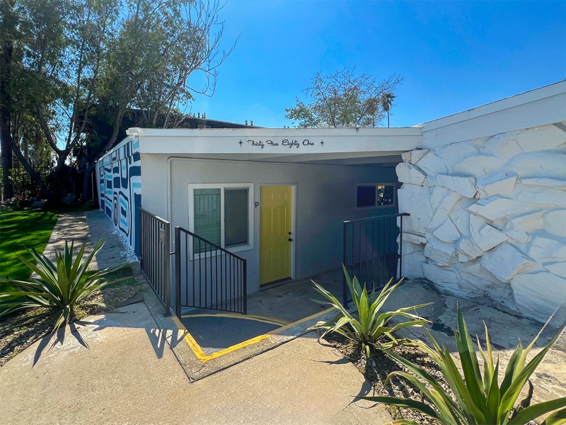 Entry walkway at 3581 Chicago Ave with the address in script above a yellow unit door, beside the rock wall and a painted mural