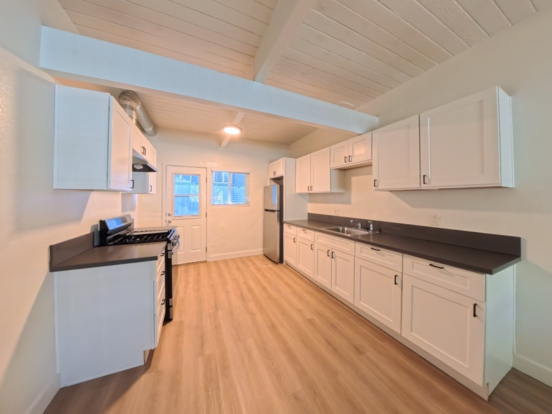 Galley kitchen with white shaker cabinets, dark counters, a stainless gas range and a back door with a window