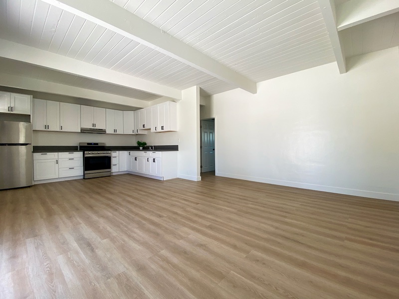 Open kitchen and living area with white cabinets along one wall, a beamed white wood ceiling and wood-look plank floors
