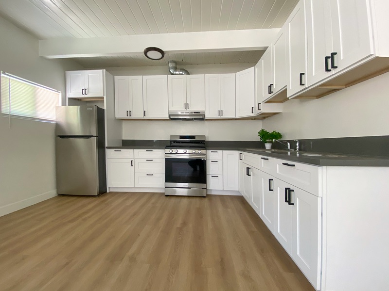 Renovated kitchen with white shaker cabinets, dark gray counters, a stainless gas range and refrigerator, and plank flooring