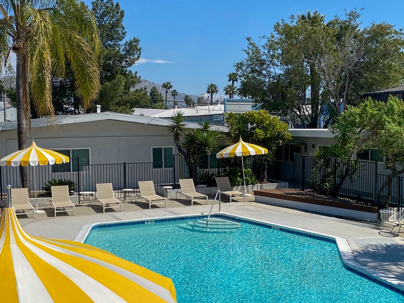 Rock Ridge pool with a striped umbrella in the foreground, lounge chairs along the fence and hills in the distance