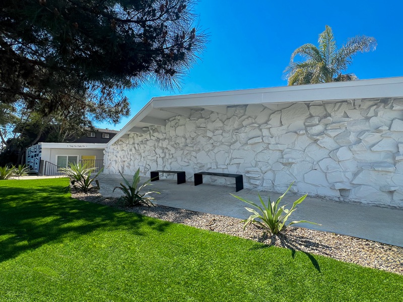White sculpted rock wall on the front of Rock Ridge with two black benches, agave plantings and a green lawn